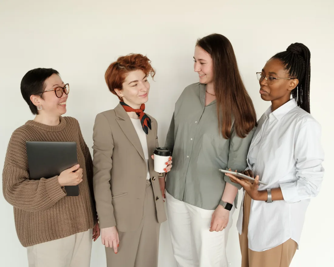 Four colleagues standing together in conversation, one holding a laptop and another a tablet